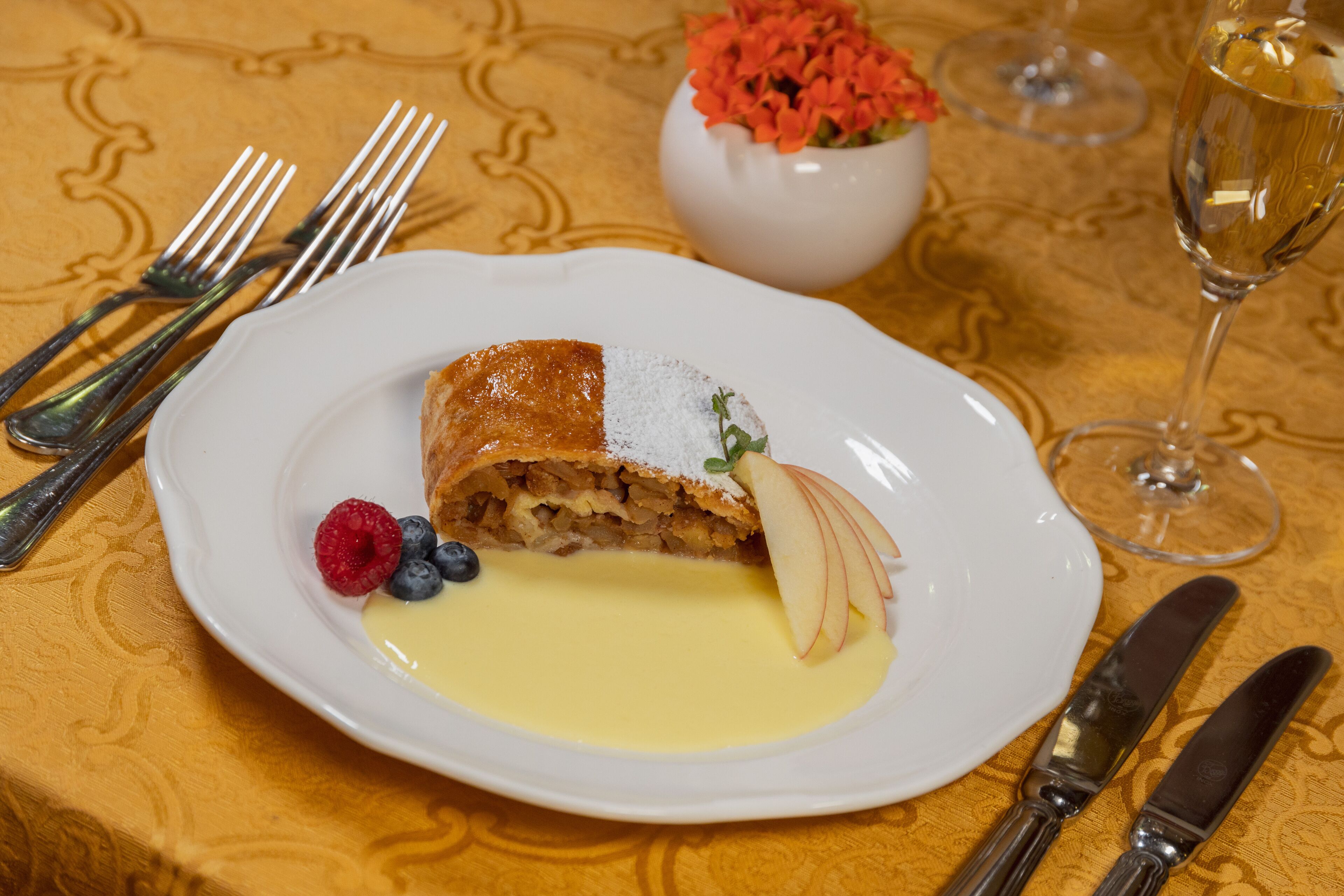 A dessert plate with a slice of cake, fruit, and sauce on a table with a patterned tablecloth.