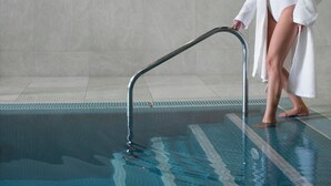A woman in a white bathrobe standing by a pool with a metal handrail. - Hotel Miravalle (San Lorenzo Dorsino)