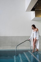 A woman in a white bathrobe standing by a pool with a metal handrail.