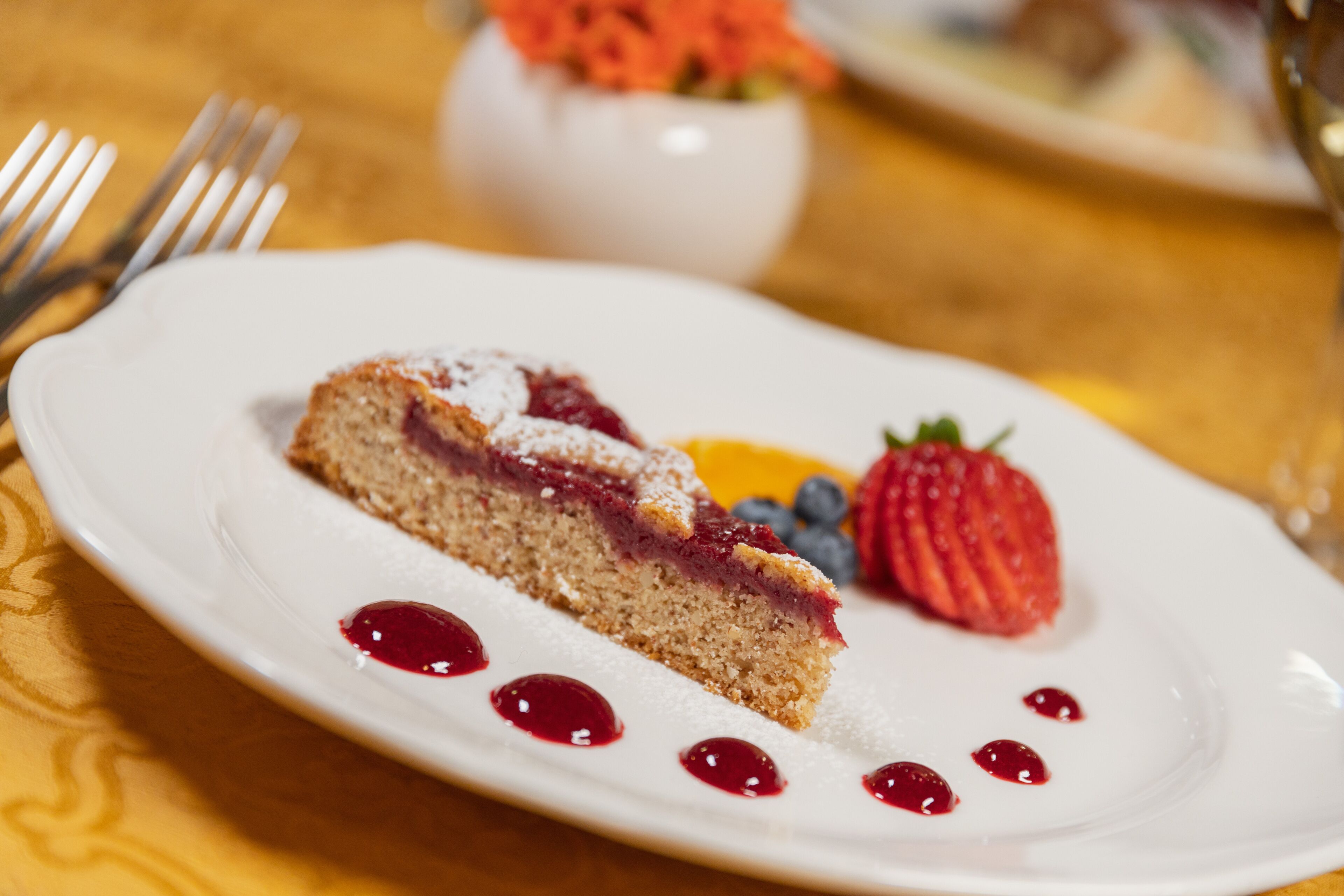 Une part de gâteau accompagnée d’une compote de fruits rouges et d’une fraise, le tout présenté sur une assiette blanche.