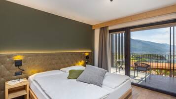 A bedroom with a large bed, a nightstand, a wall-mounted lamp, and a view of a balcony with a chair and table.