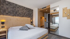 A modern bedroom with a large bed, wooden headboard, and a mirror reflecting the room. - Hotel Miravalle (San Lorenzo Dorsino)