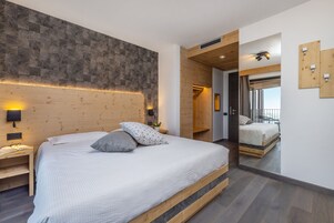 A modern bedroom with a large bed, wooden headboard, and a mirror reflecting the room.