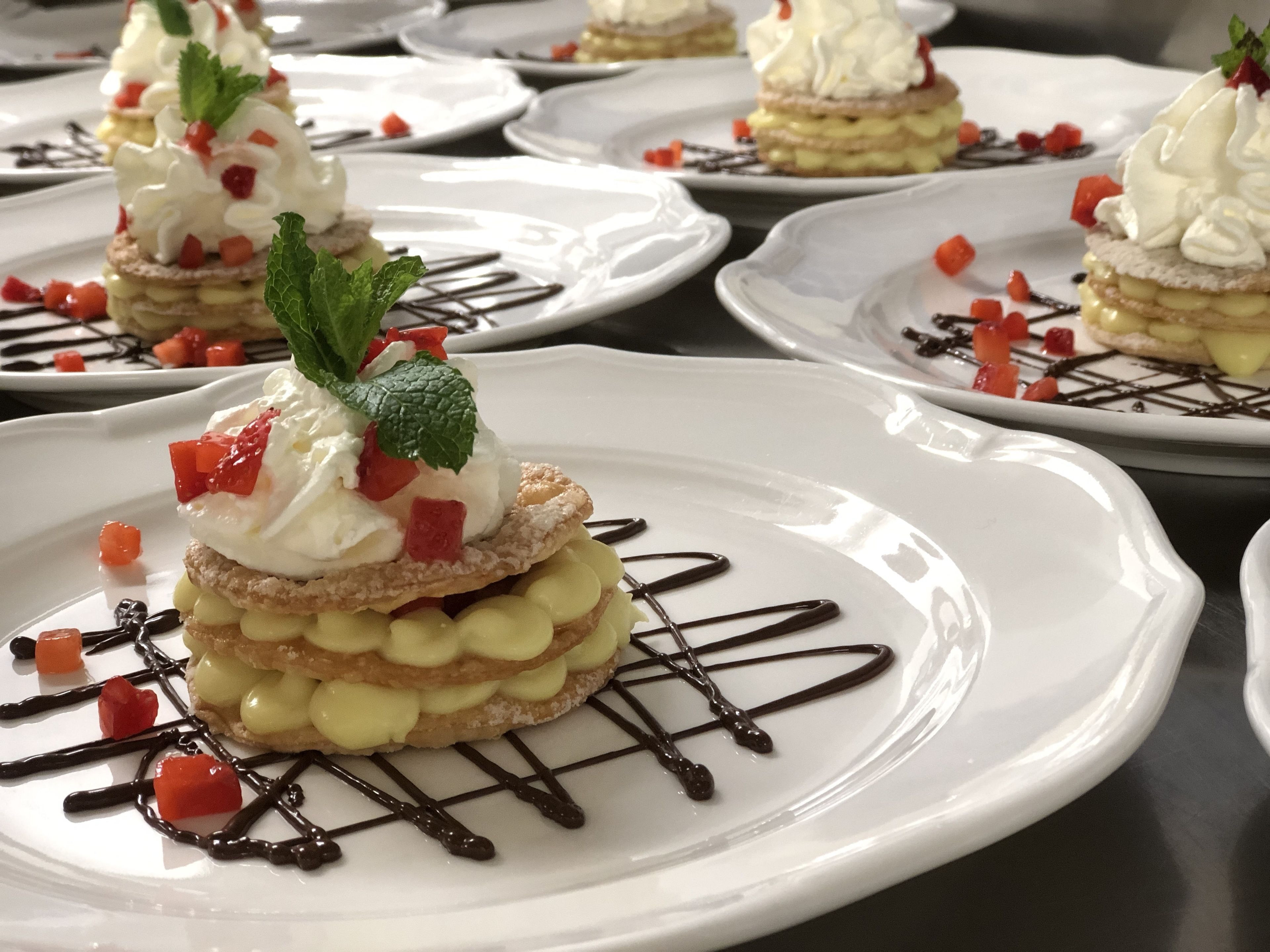 Presentación de postres con varias fuentes, cada una con un pastel en capas, crema batida, menta y un chorrito de chocolate.
