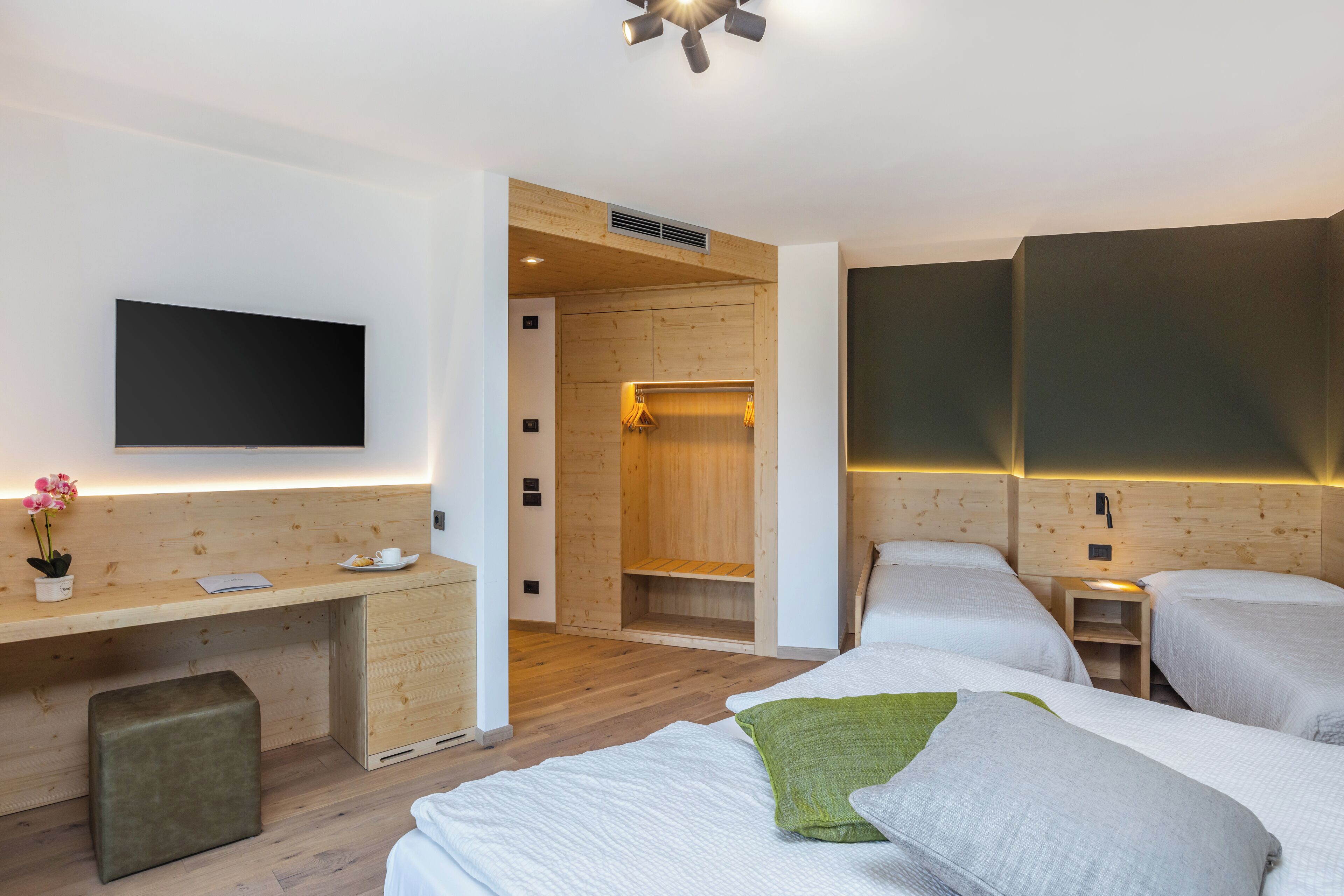 Una habitación de hotel moderna con un escritorio de madera, un televisor de pantalla plana, dos camas y un vestidor.