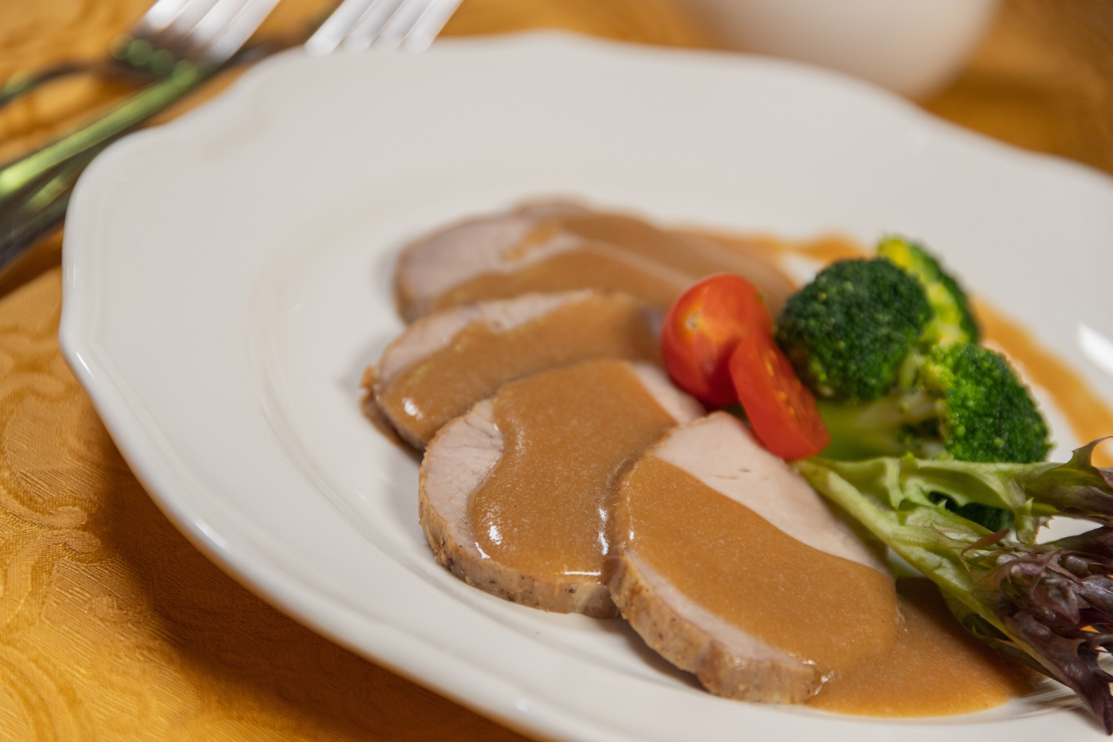 A plate with slices of meat, gravy, broccoli, and cherry tomatoes.