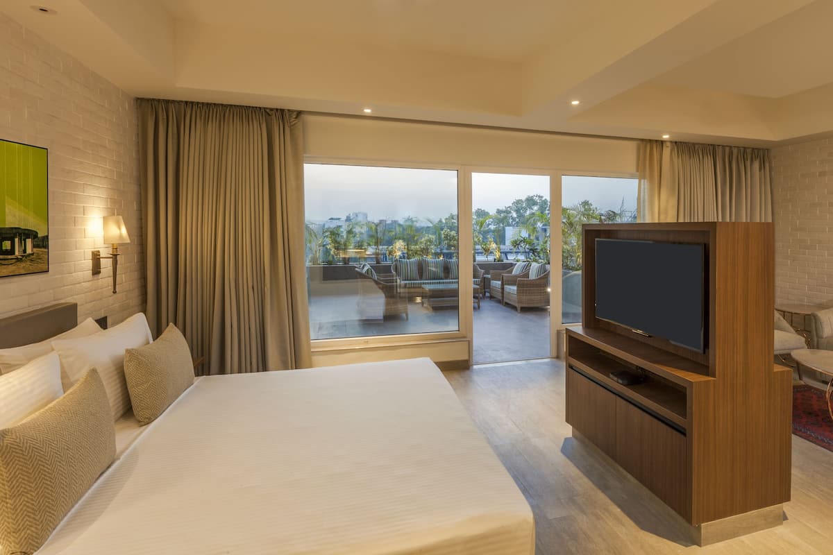 A hotel room with a large bed, a TV, a sofa, and a balcony with a view of the city.