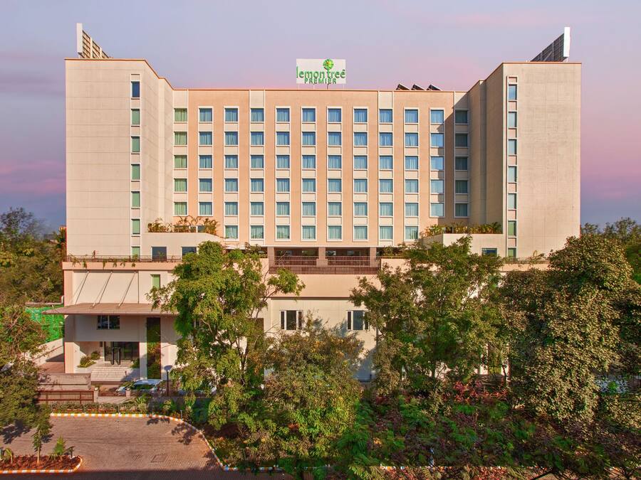 Un gran edificio de hotel con varios pisos, un letrero llamativo y abundante vegetación alrededor.