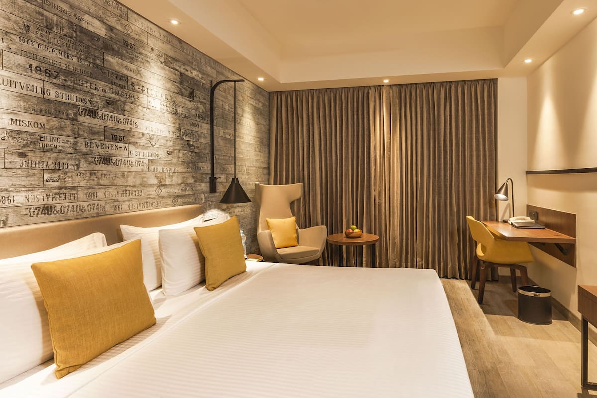 A hotel room with a large bed, a desk, a chair, a TV, and a wall with vintage-style text.