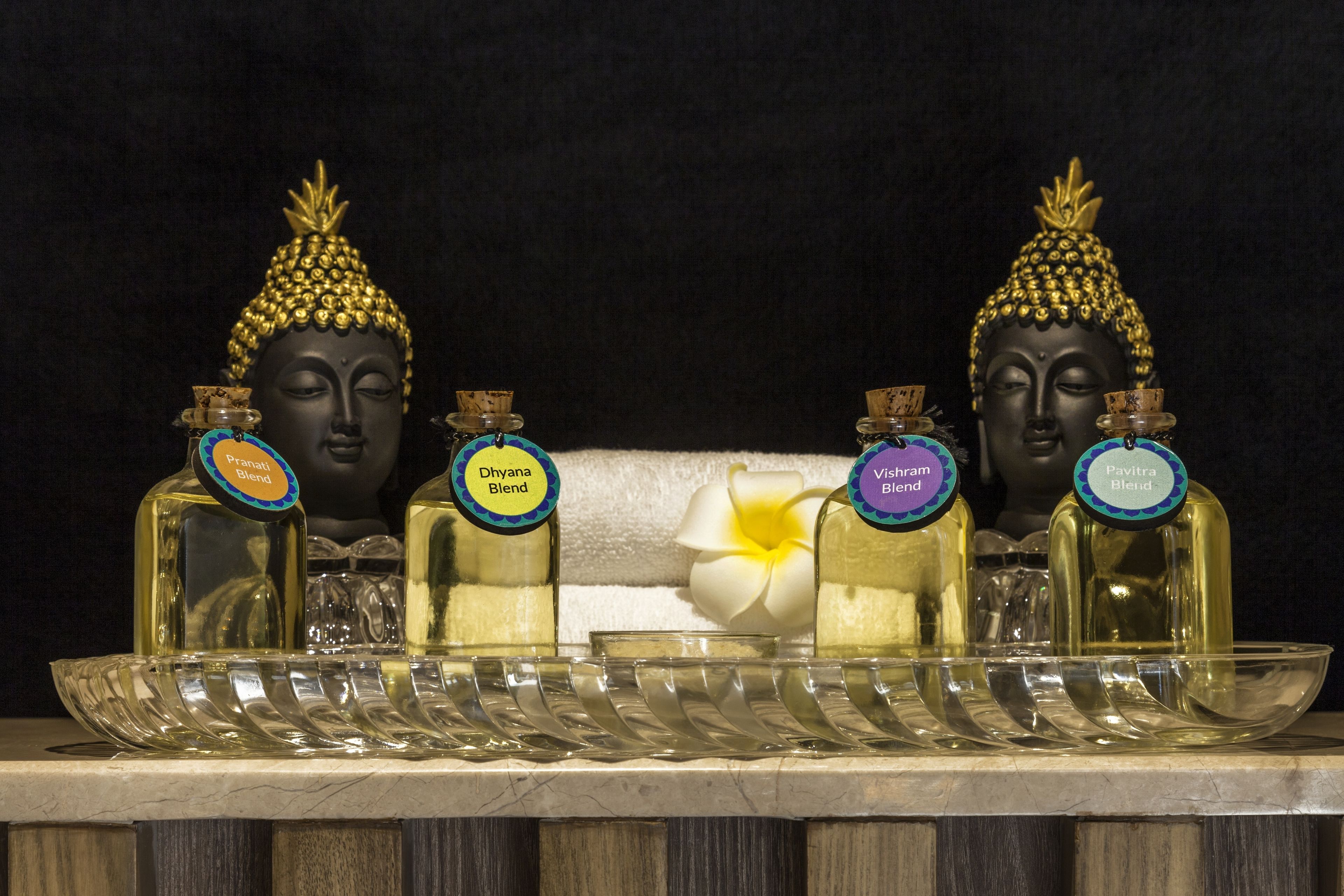 A display of four Buddha statues with labeled bottles of essential oils in front of them.