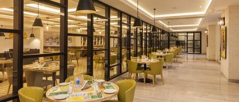 Un espace de restauration moderne avec des tables rondes, des chaises vertes et des luminaires suspendus.