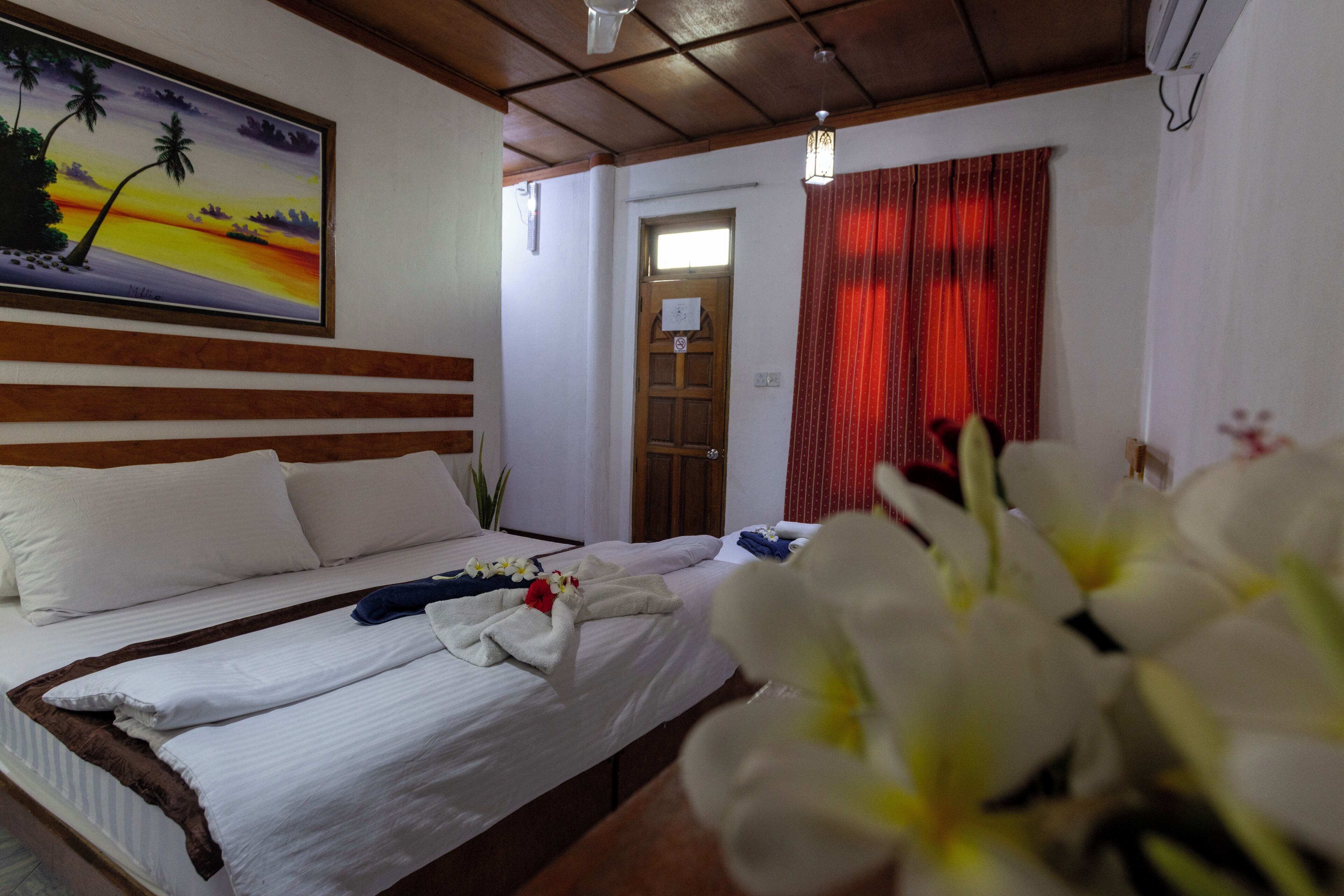 Una camera d'albergo con un letto, un quadro raffigurante un tramonto, una testiera in legno e una tenda rossa.