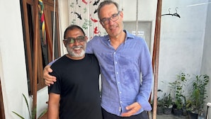 Two men standing in a courtyard with a brick floor, potted plants, and a wooden structure. - Goby Lodge Guest House (Mahibadhoo)