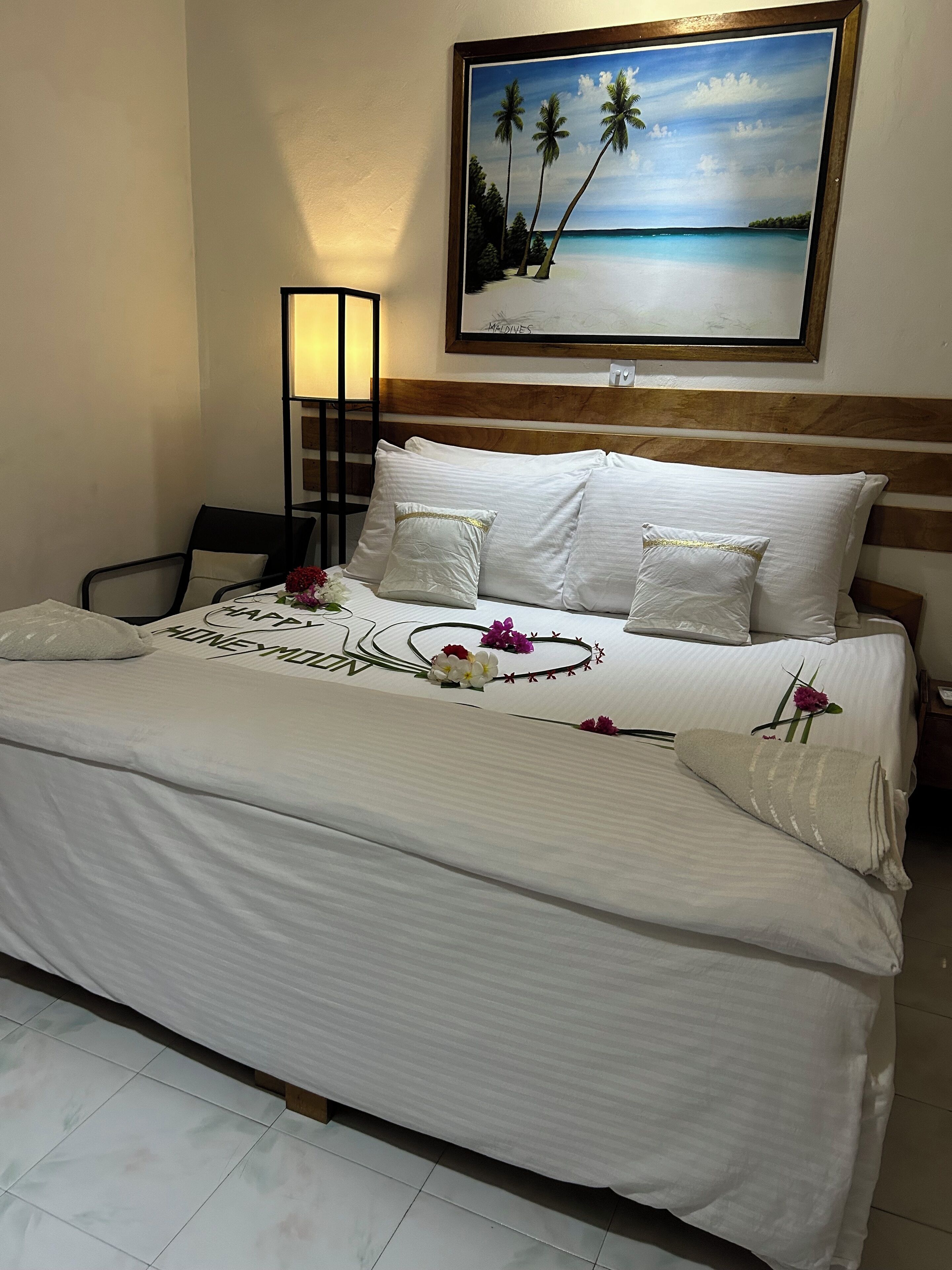 Una habitación de hotel con una cama, un cuadro de una escena de playa y una mesita de noche con una lámpara.