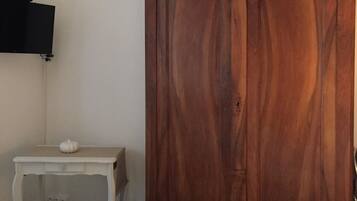 A bedroom with a wooden wardrobe, a small bedside table with a white object, and a bed with folded white linens.