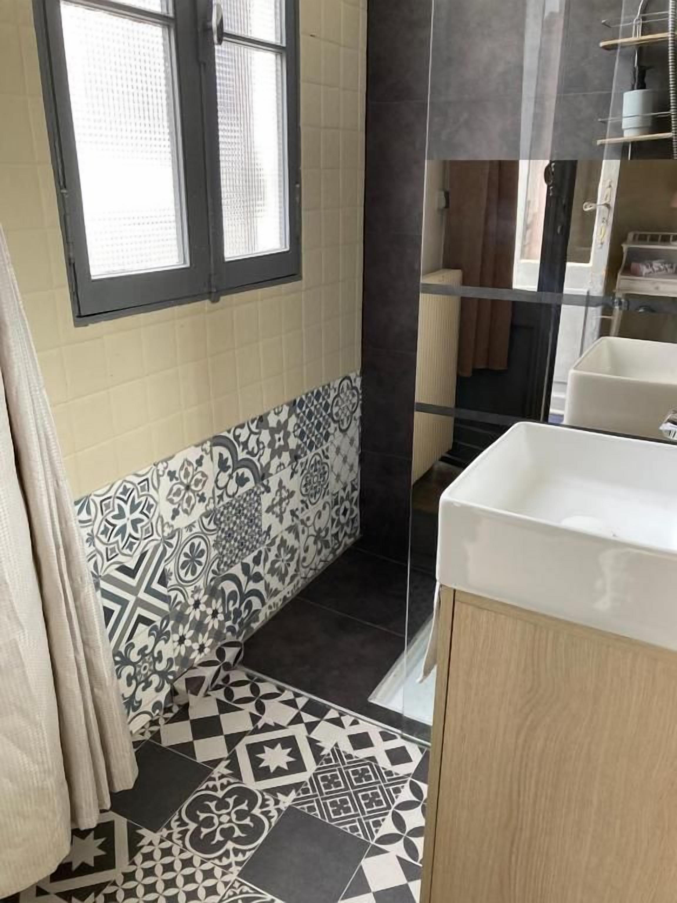 A bathroom with patterned tiles, a window, and a sink.