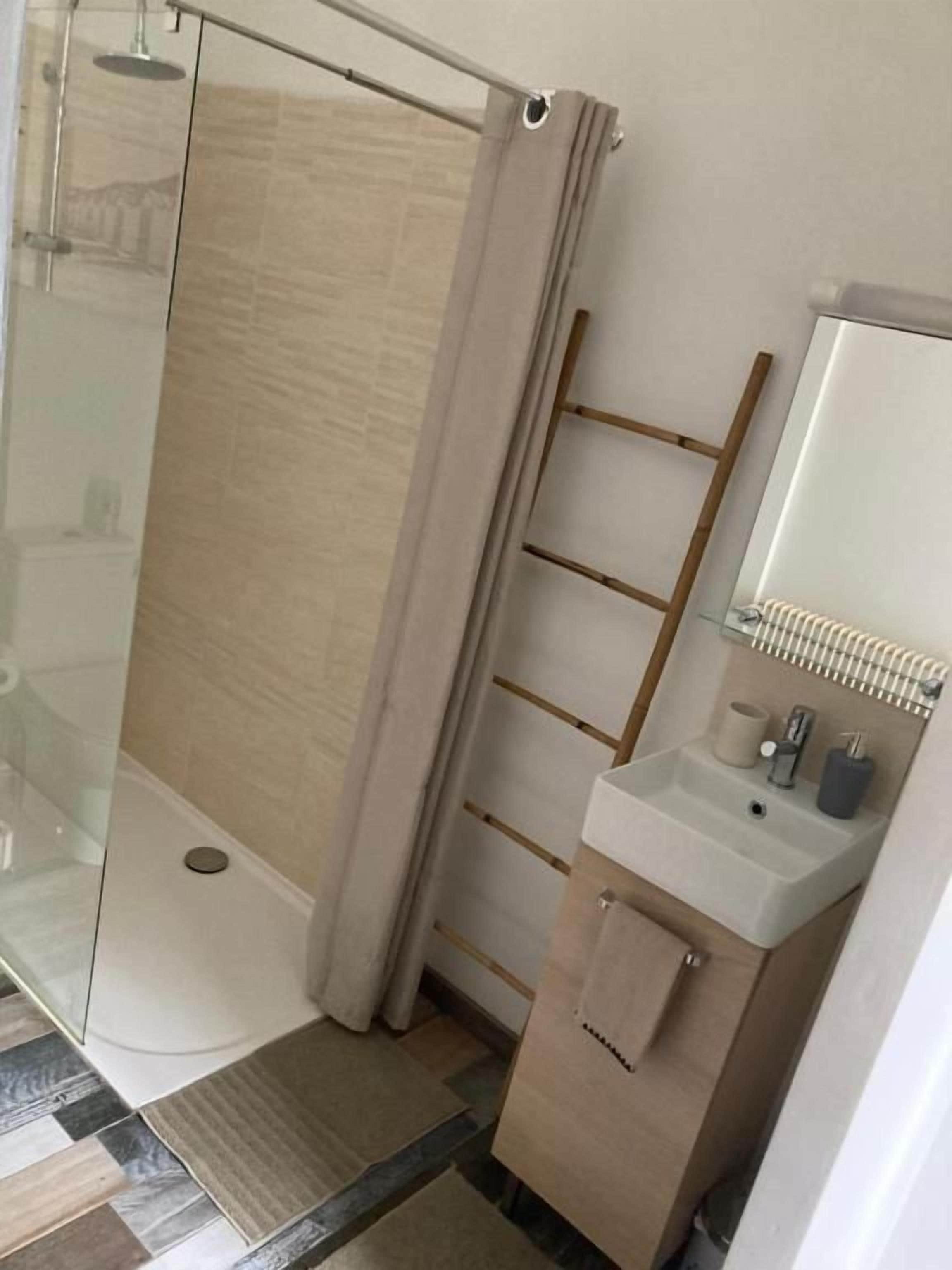 Un baño con cabina de ducha de vidrio, una estantería de escalera de madera, un lavabo con espejo y un perchero para toallas.