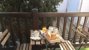 A wooden deck with a table set for breakfast, including bread, butter, and beverages. - Villa des T (Arcachon)