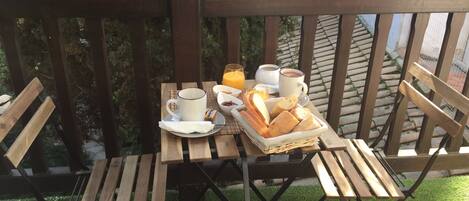 A wooden deck with a table set for breakfast, including bread, butter, and beverages.