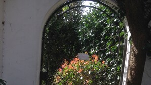A metal gate with a sign, surrounded by greenery and a tree. - Villa des T (Arcachon)