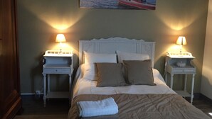 A neatly made bed with pillows, two bedside tables with lamps, and a painting of a boat on the wall. - Villa des T (Arcachon)