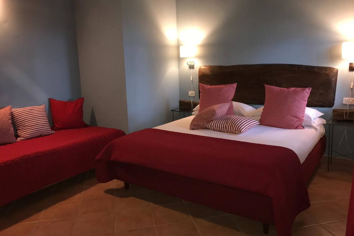 Une chambre d’hôtel avec deux lits, chacun agrémenté de draps et d’oreillers rouges assortis. On y trouve deux tables de chevet fixées au mur, chacune équipée d’une lampe.