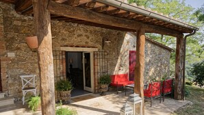 Un edificio de piedra con una pérgola de madera, asientos al aire libre y plantas en macetas.