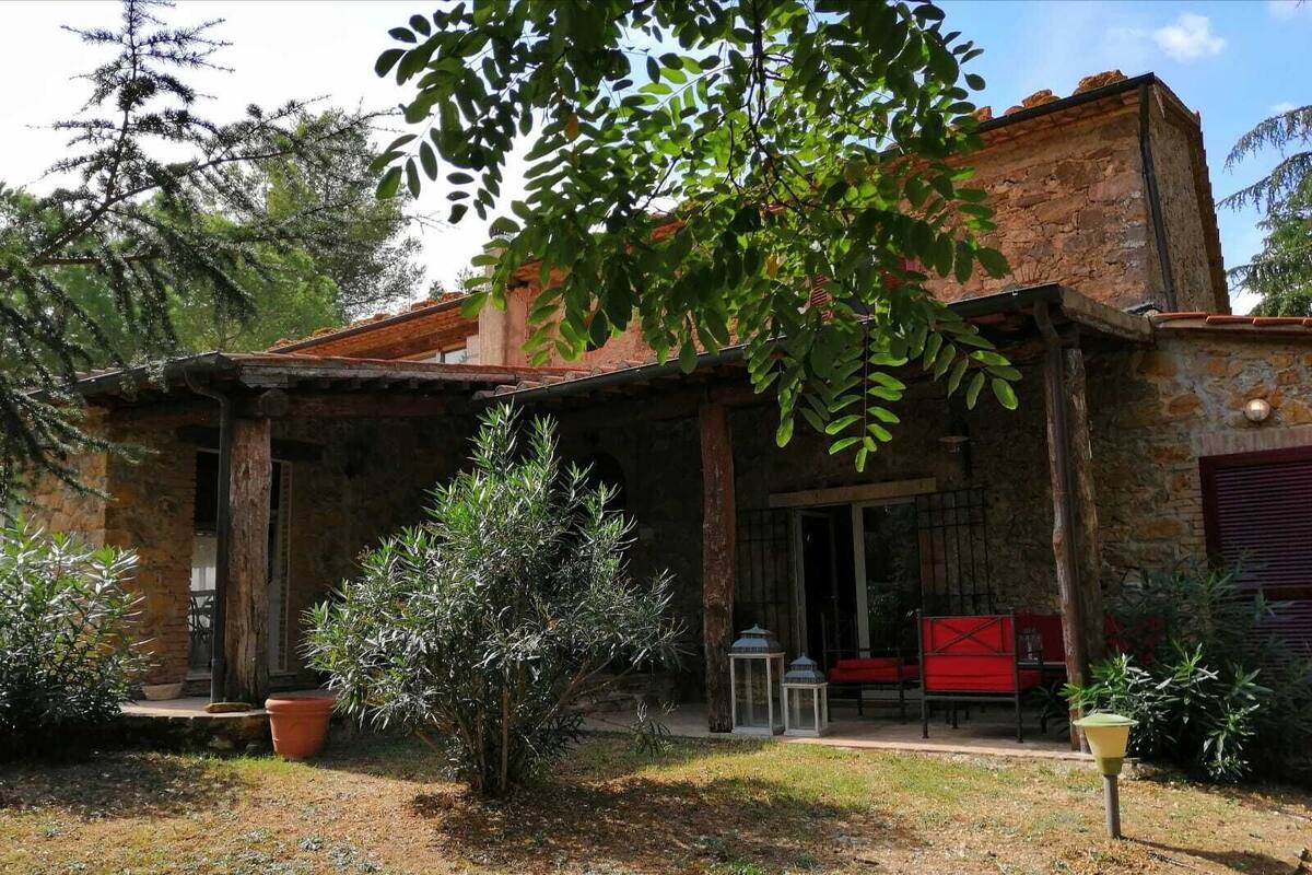 Un bâtiment rustique en pierre, doté d’un porche couvert, de plantes en pot et d’un petit jardin.