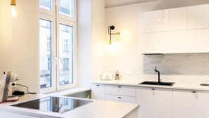 A modern kitchen with white cabinets, a black countertop, a built-in stove, and a window with a view of buildings outside. - Faust and Mona Lisa Apartments (Kraków)