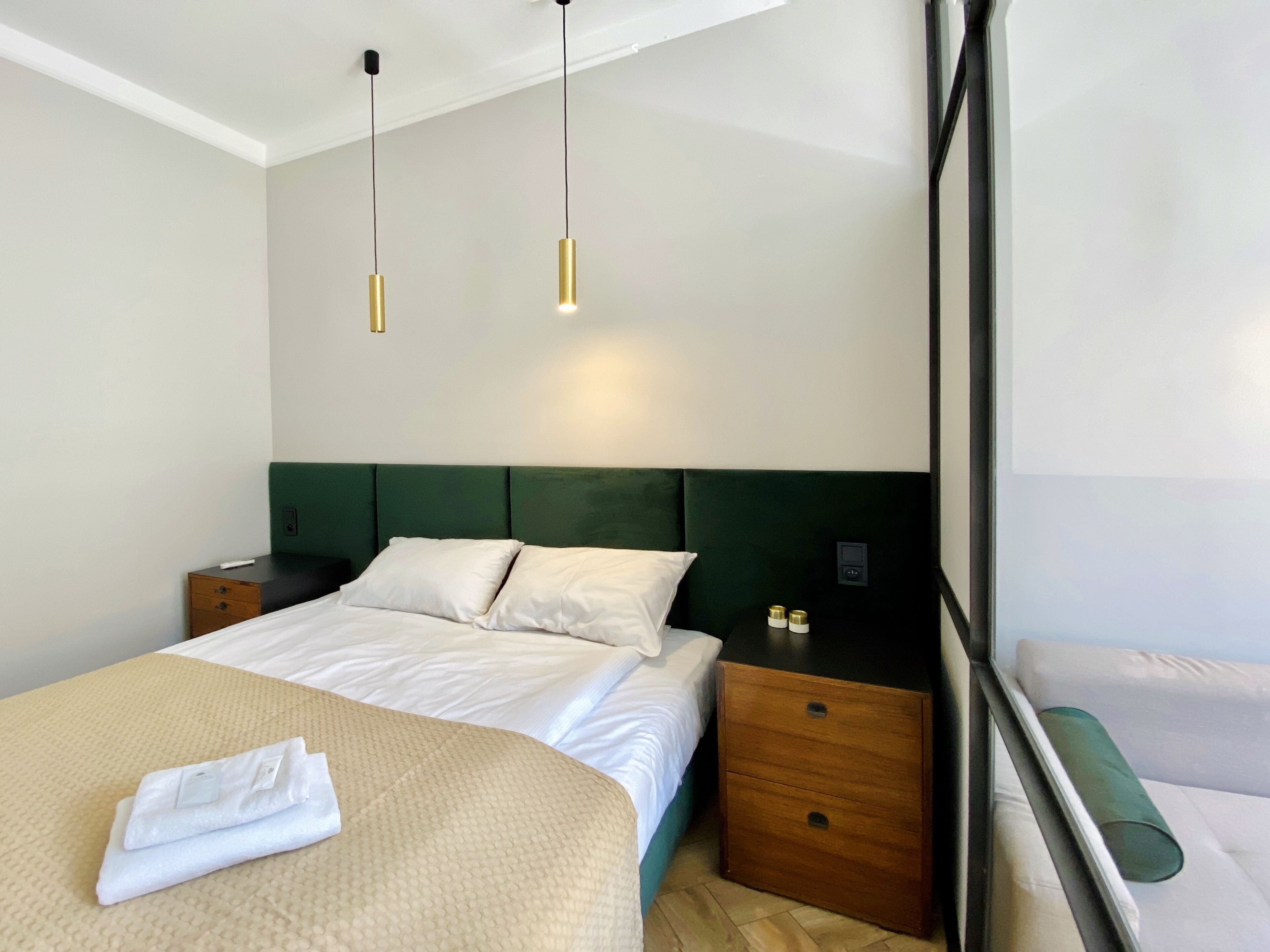 A hotel room with a bed, bedside tables, a green headboard, and pendant lights.