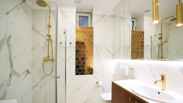 A modern bathroom with a glass-enclosed shower, a marble-tiled wall, a wooden vanity, and a gold faucet. - Faust and Mona Lisa Apartments (Kraków)