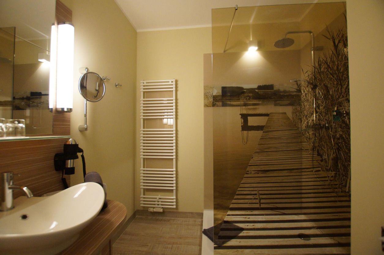 Ein modernes Badezimmer mit Waschbecken, Spiegel, Handtuchhalter und einer Glasabtrennung mit Blick auf eine Holzterrasse.