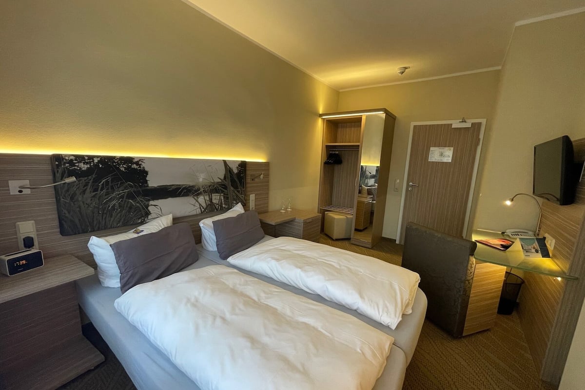 Ein Hotelzimmer mit einem großen Bett, Nachttischen, einem Fernseher und einem Spiegel.