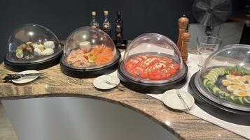 A buffet table with various food items covered in clear domes, including cheese, smoked salmon, and sliced tomatoes.
