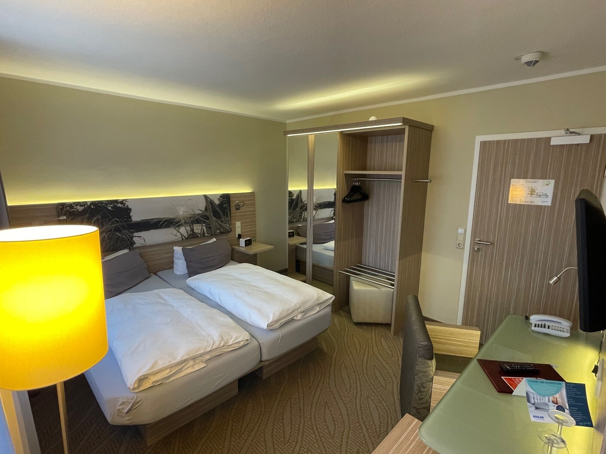 Una habitación de hotel con cama, mesita de noche, lámpara y espejo.