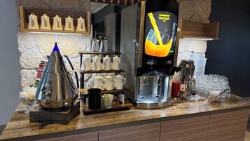 Een koffiehoek met een koffieapparaat, een waterkoker en verschillende mokken en glazen.