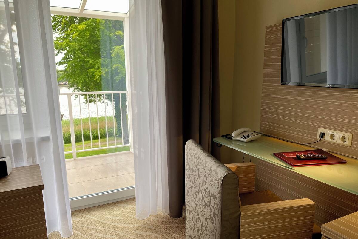 Ein Hotelzimmer mit Glastür zum Balkon, einem Schreibtisch mit Telefon und einem an der Wand montierten Fernseher.
