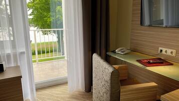 A hotel room with a glass door leading to a balcony, a desk with a telephone, and a television mounted on the wall.