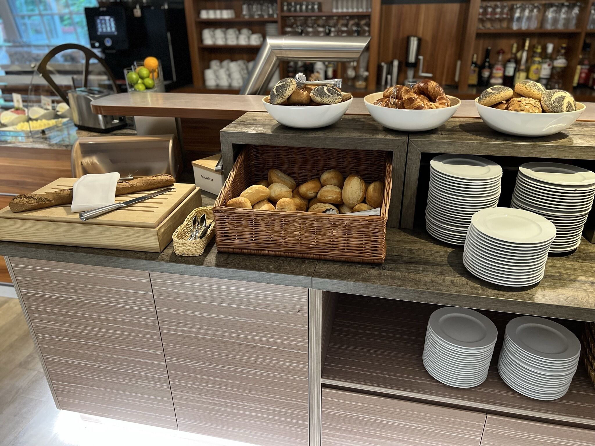 A buffet setup with bread, pastries, and stacked plates.