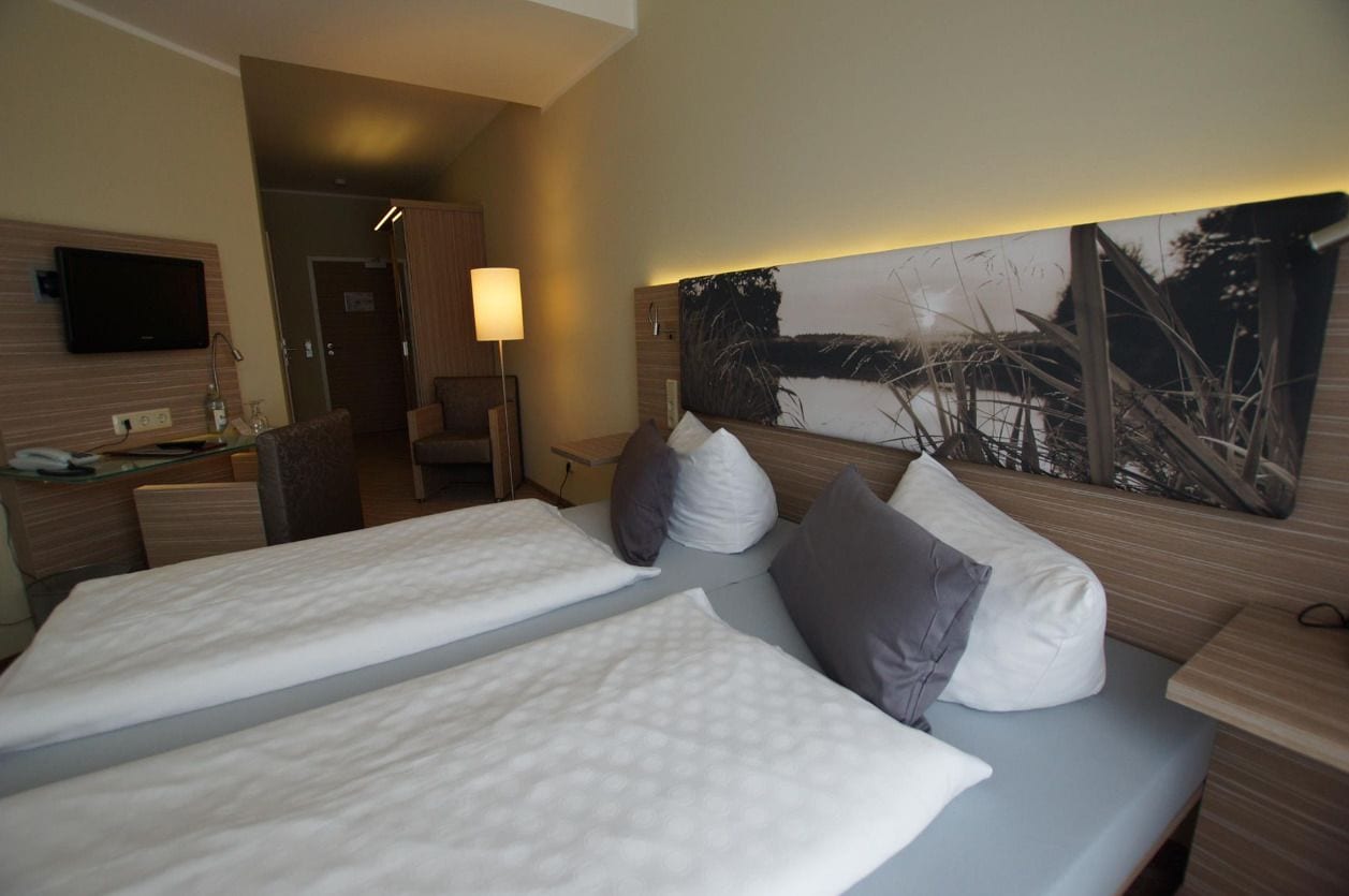 A hotel room with two beds, a flat-screen TV, a desk with a lamp, and a large painting on the wall.