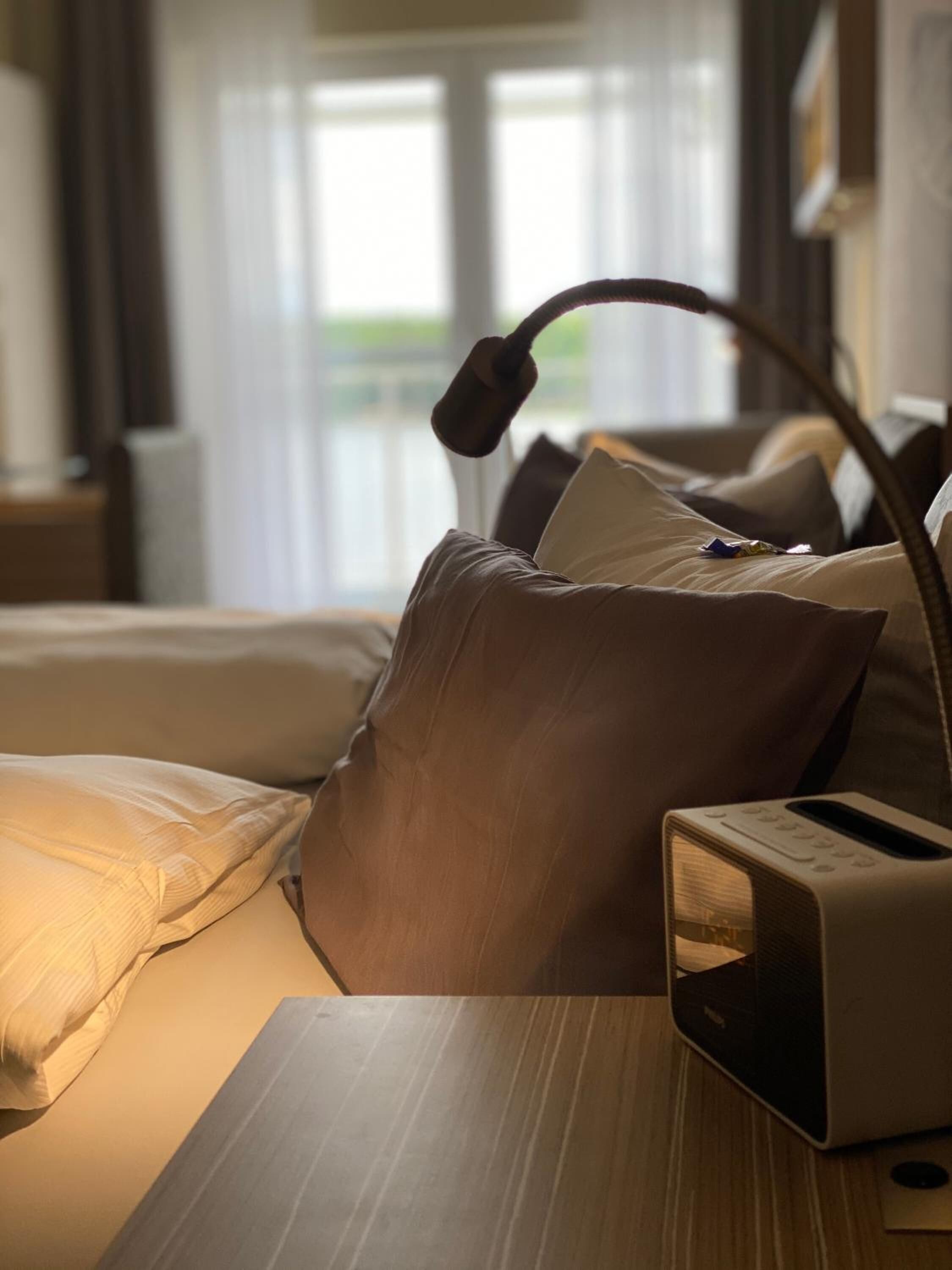 A neatly made bed with a bedside table, a lamp, and a radio.