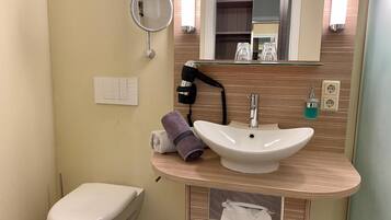 Ein Badezimmer mit Toilette, rundem Spiegel, Waschbecken mit Armatur und Handtuchhalter.