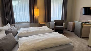 Hotellihuone, jossa on sänky, tuoli, työpöytä ja televisio.
