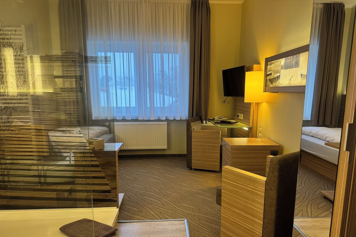 Ein Hotelzimmer mit Bett, Schreibtisch, Sessel, Sofa, Lampe und Fernseher.