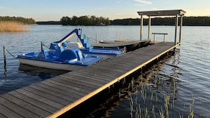 Un moll de fusta que s'endinsa en aigües tranquil·les, amb una zona coberta per seure i una barca amarrada al final.