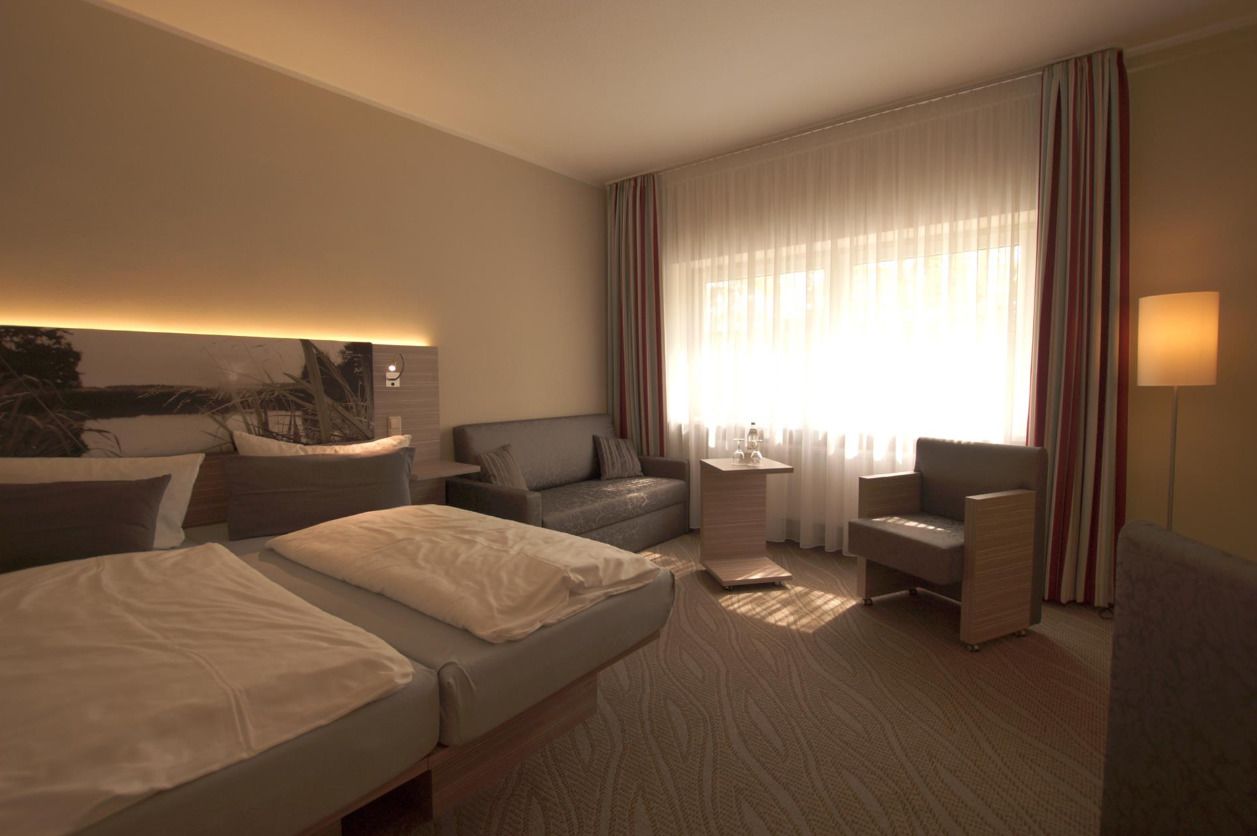 Habitación de hotel con dos camas, un sofá, una silla, una mesita y una lámpara.