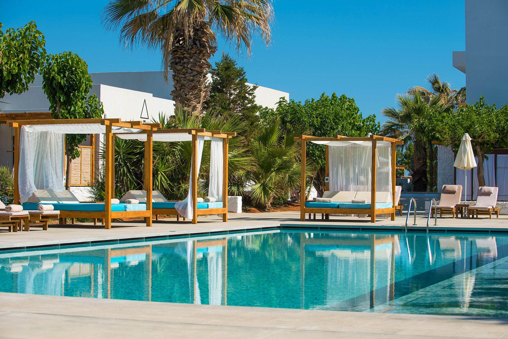 Ein Poolbereich mit zwei hölzernen Baldachinbetten, Liegestühlen und einem klaren, blauen Pool.