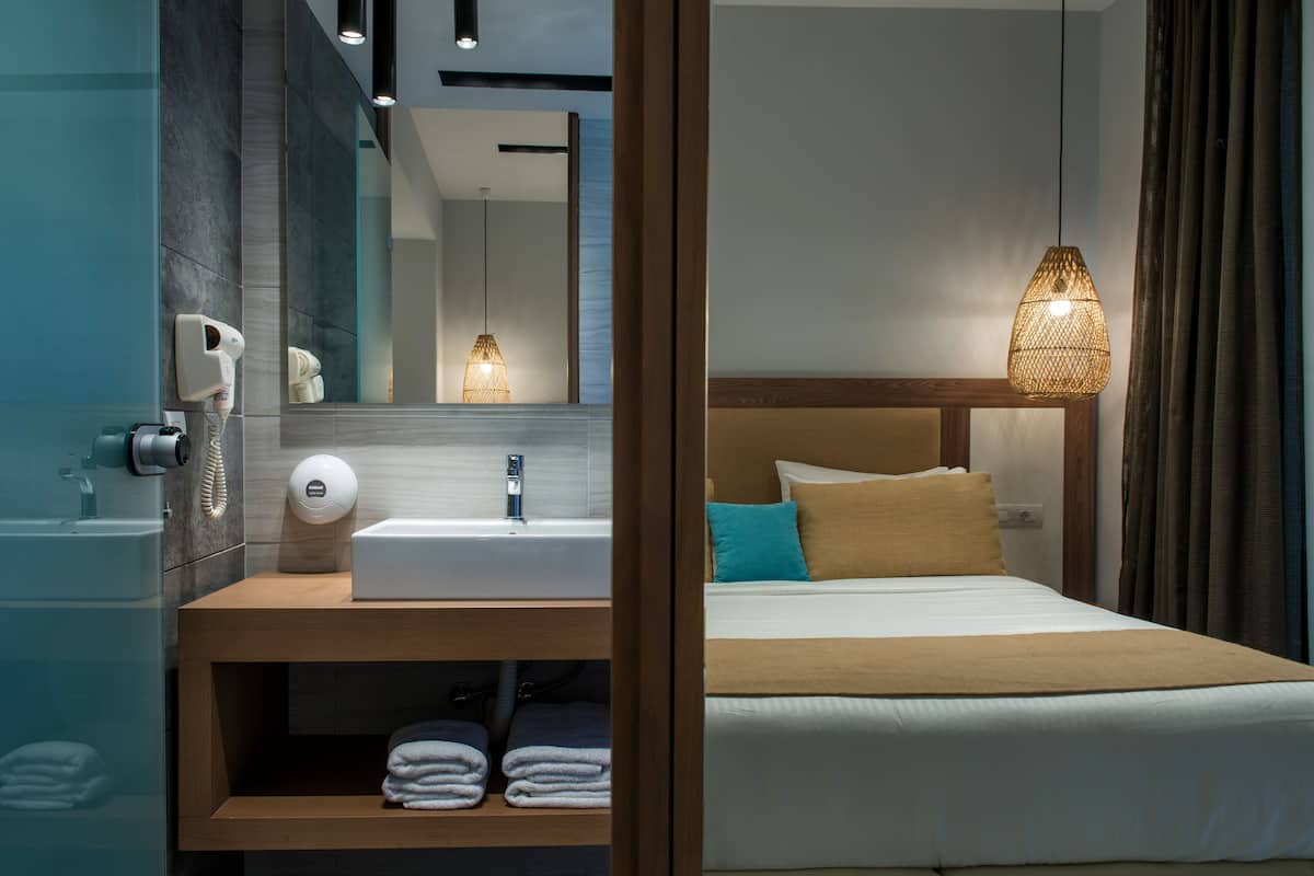 Ett modernt hotellrum med en sminkbord i trä, en stor spegel, ett vitt handfat och en säng med en sänggavel.