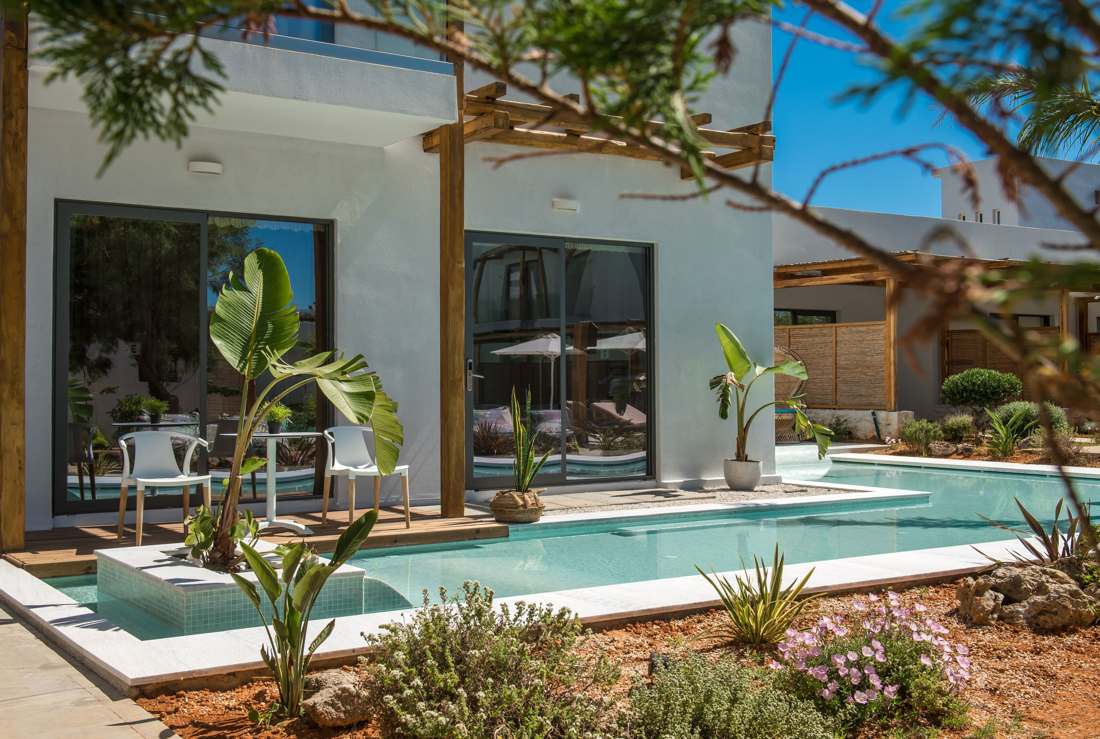 A modern outdoor pool area with a pergola, seating, and potted plants.