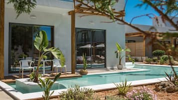 A modern outdoor pool area with a pergola, seating, and potted plants.